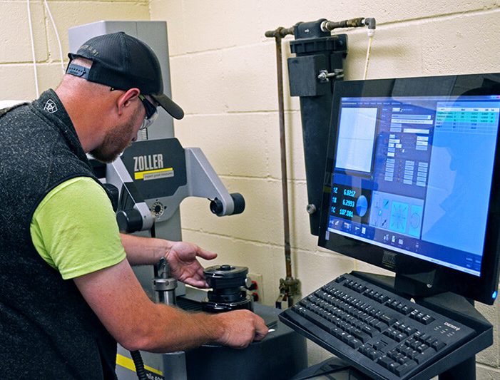 An electromechanical technician calibrates production and manufacturing equipment using both a computer control interface and hands-on manual adjustments to the machinery