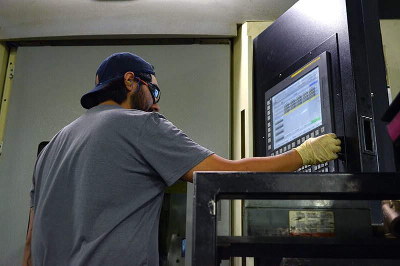 A young mechatronics technologist uses a digital panel to maintain and operate industrial machining equipment