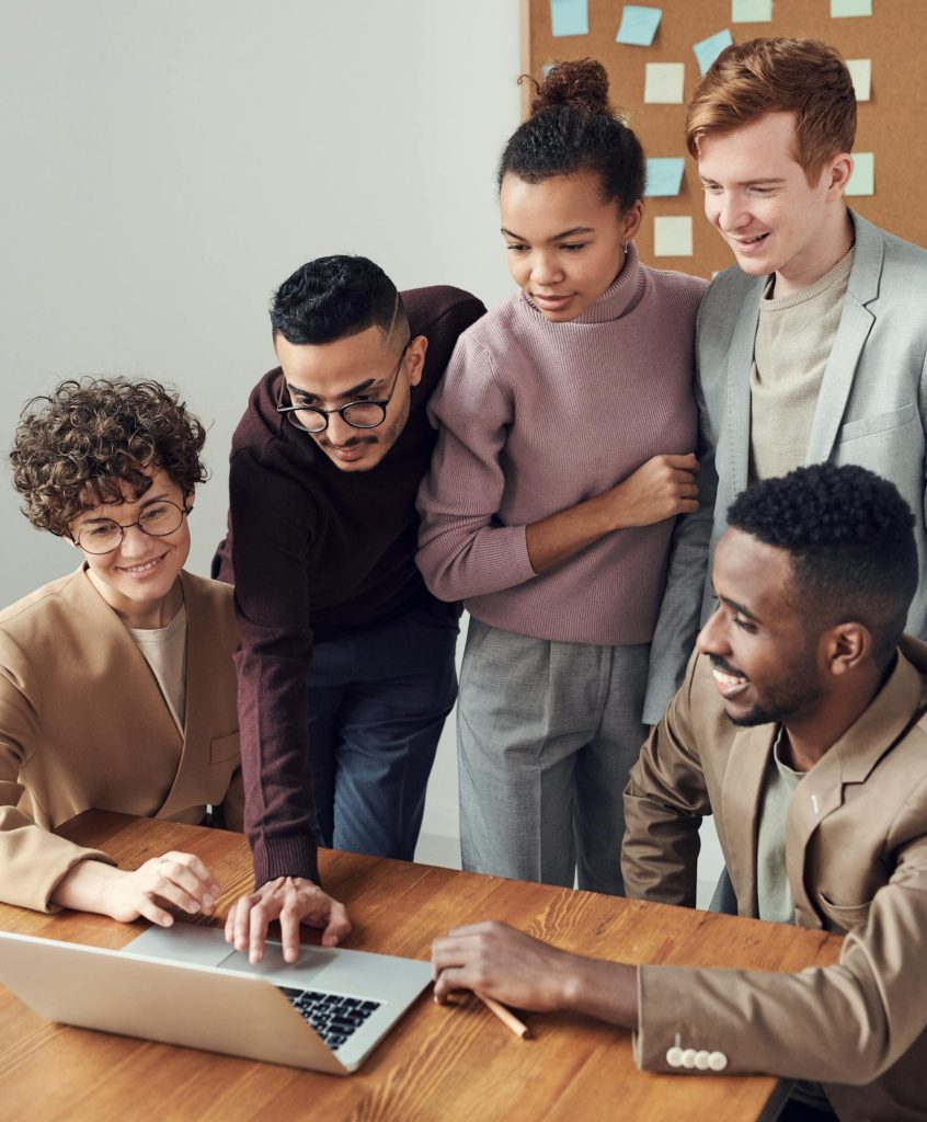 A group of smiling students or young workers gathered around a computer in interest