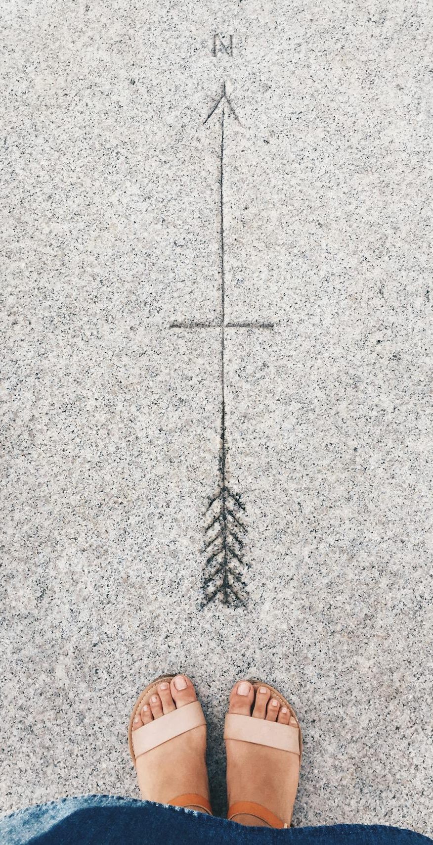 A person standing before a compass pointing north etched into the sidewalk