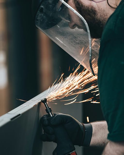 Man in protective mask works as metal cutter or grinder in welder shop