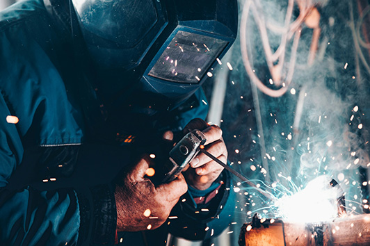 Professional welder in welder's mask working as a pipeline welder indoors